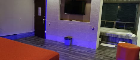 A modern hotel room with a large bed, a flat-screen TV mounted on the wall, a small trash bin, and a window with a view of the sea.