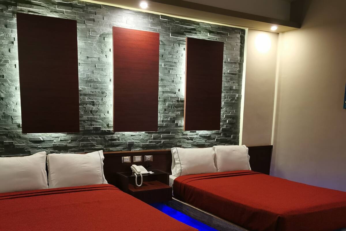 A hotel room with two beds, a phone on a bedside table, and a wall with a stone-like texture.