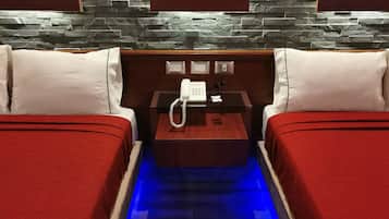 Habitación de hotel con dos camas, una mesita de noche de madera, un teléfono y una pared de piedra.