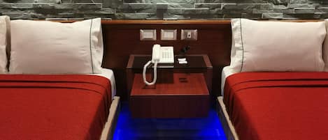Habitación de hotel con dos camas, una mesita de noche de madera, un teléfono y una pared de piedra.