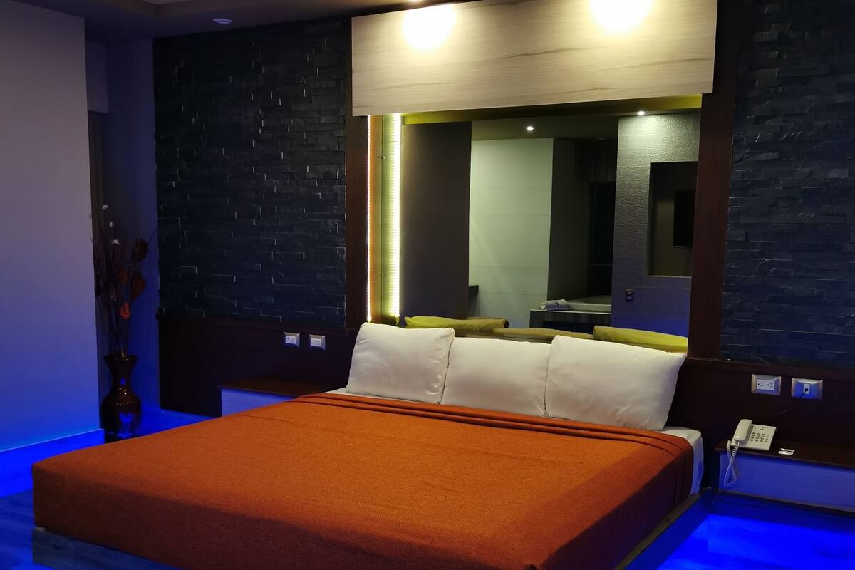 A modern bedroom with a large bed, a bedside table, a mirror, and a nightstand.