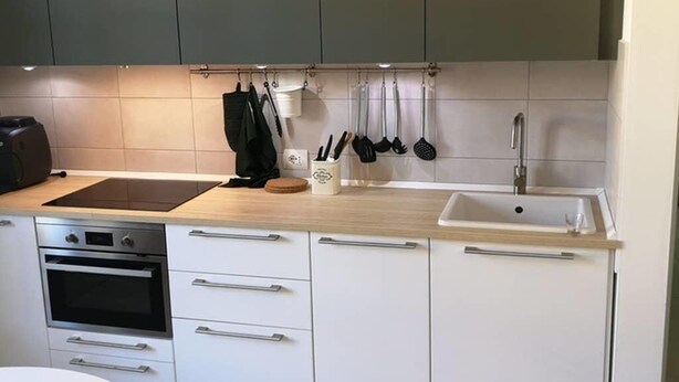 A modern kitchen with white cabinets, a built-in oven, a sink, and various utensils hanging on the wall. - Two-room apartment overlooking the Basilica (Loreto)