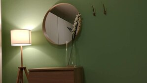A room with a wooden dresser, a round mirror, a floor lamp, and a vase with flowers on the wall. - Two-room apartment overlooking the Basilica (Loreto)