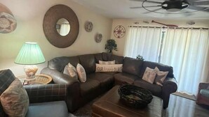 A living room with a sofa, ottoman, and a ceiling fan. - Location! Location! Townhouse.    STR Permit #: 040846 (Hilton Head)