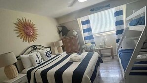A bedroom with a bunk bed, a ceiling fan, a sun decoration, a wooden cabinet, and a window with curtains. - Location! Location! Townhouse.    STR Permit #: 040846 (Hilton Head)