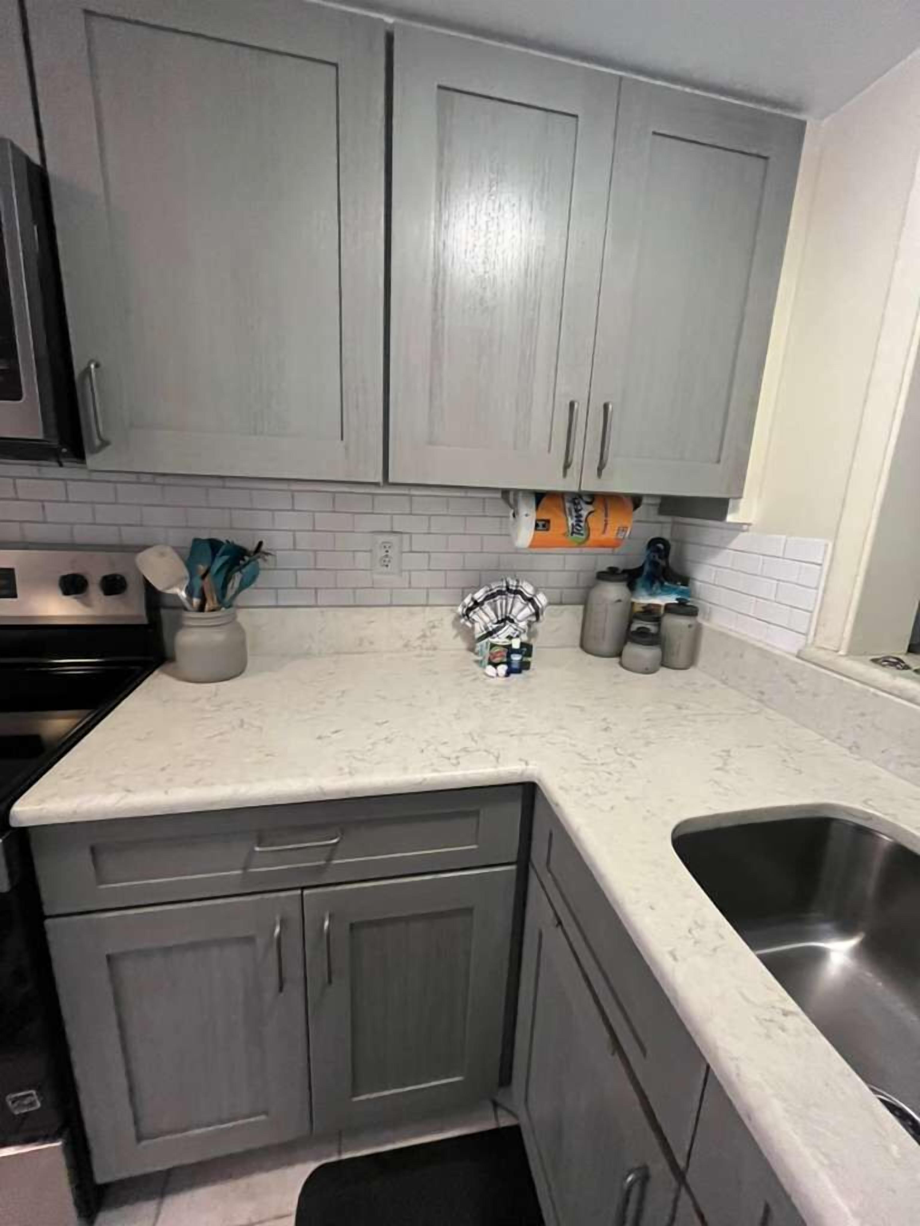 Una cocina con gabinetes grises, una encimera blanca y un fregadero de acero inoxidable.