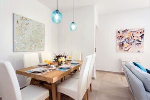 A dining area with a wooden table set for four, white chairs, and two hanging blue pendant lights. - Ionian Sun - Holiday Home with Sea View (Corfu)