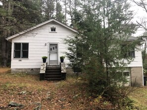 Standalone cottage surrounded by a natural setting with trees and shrubs.