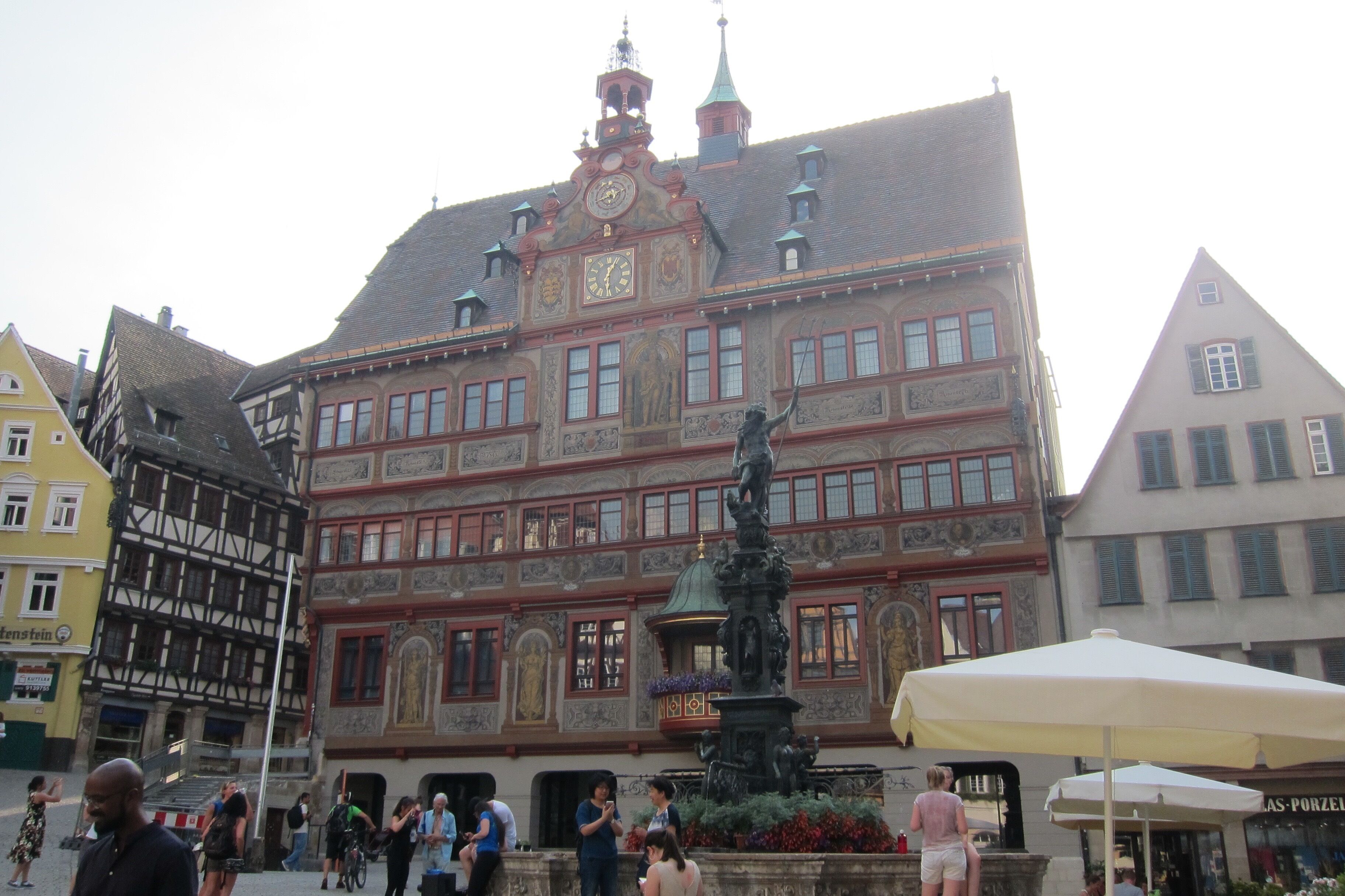Ein historisches Gebäude mit einem Glockenturm, einer Statue und einem Brunnen davor.