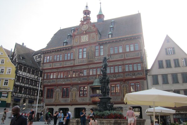Un edificio histórico con una torre del reloj, una estatua y una fuente en su parte frontal.