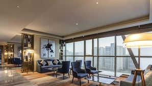 A spacious living area with a large window, a sofa, armchairs, a coffee table, and a floor lamp. - Novotel Zhengzhou Airport (Zhengzhou)