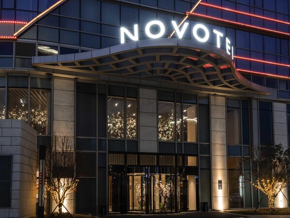 Ein moderner Hotel Eingang mit einem gut sichtbaren 'NOVOTE'-Schild, großen Glasfenstern und einer gut beleuchteten Fassade.