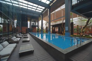Une piscine intérieure dotée de chaises longues et d’un plafond en verre.