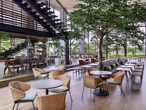 A modern outdoor cafe with wicker furniture, glass walls, and a staircase.