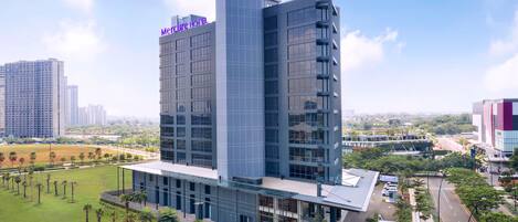 A modern hotel with a prominent 'Mefcure Hotel' sign, surrounded by a well-maintained lawn and palm trees.