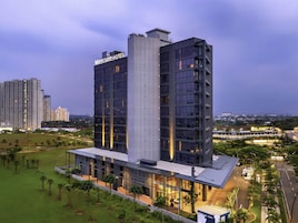 Um hotel moderno com uma placa de destaque, vários andares e uma área ao redor bem cuidada.