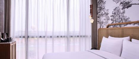 A hotel room with a large bed, a desk with a telephone, and a wall with a tree mural.