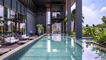 Una piscina interior moderna con agua cristalina, rodeada de sillones de descanso y plantas en macetas.
