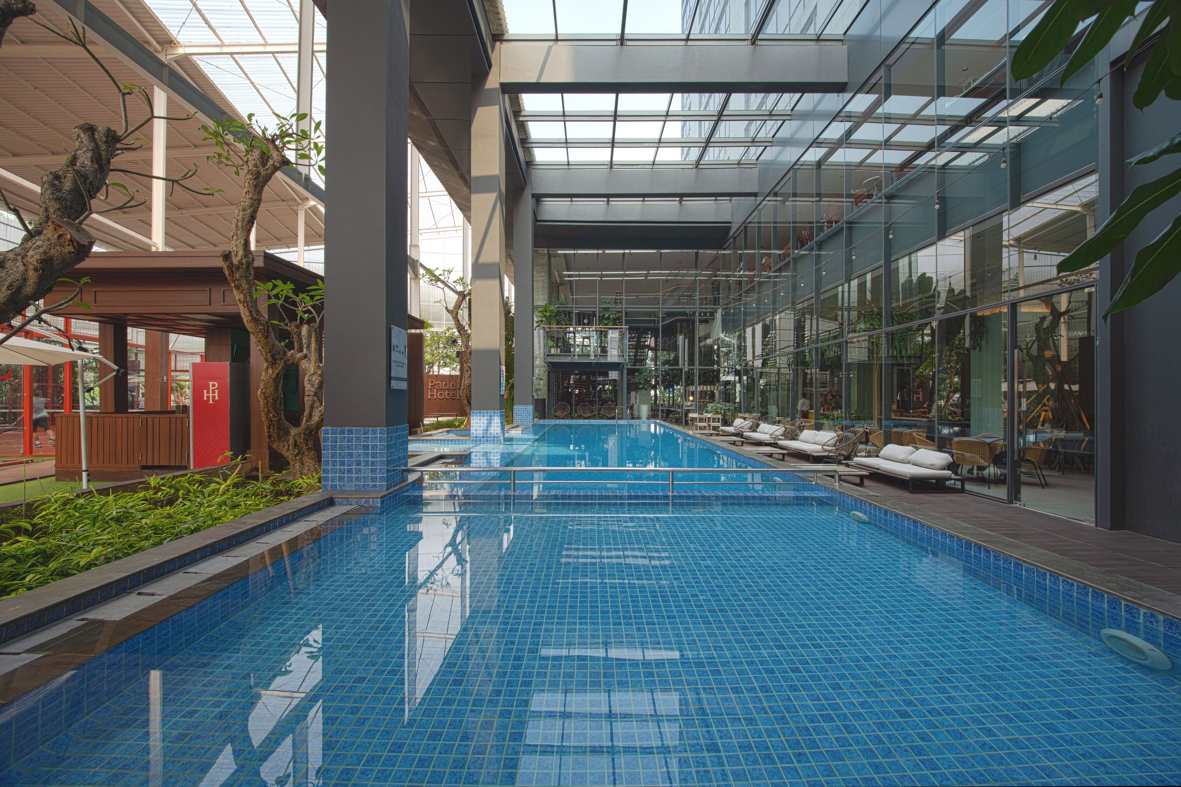 An indoor swimming pool with clear blue water, surrounded by lounge chairs and a glass wall reflecting the interior.