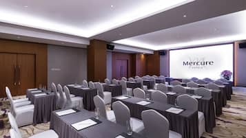 A conference room with rows of tables and chairs, a large screen displaying 'Mercure Hotels', and a wooden door in the background.