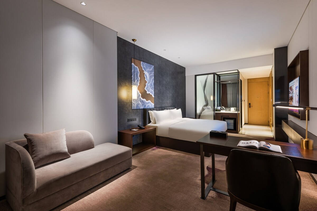 A modern hotel room with a sofa, a bed, a desk, and a large mirror.