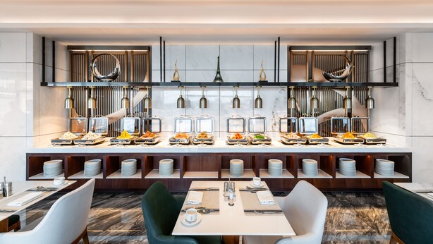 A modern hotel dining area with a buffet setup, multiple dining tables, and a central decorative feature resembling the Eiffel Tower. - Shenzhen Longgang Kunyi Mercure Hotel (Shenzhen)