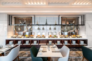 A modern hotel dining area with a buffet setup, multiple dining tables, and a central decorative feature resembling the Eiffel Tower. - Shenzhen Longgang Kunyi Mercure Hotel (Shenzhen)