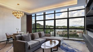 A modern living room with a sectional sofa, a round coffee table, and a large window offering a city view. - Shenzhen Longgang Kunyi Mercure Hotel (Shenzhen)