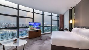A hotel room with a large window, a bed, a TV, a small table, and a sofa. - Shenzhen Longgang Kunyi Mercure Hotel (Shenzhen)