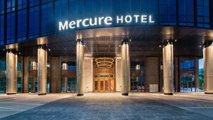The exterior of the Mercure Hotel with a modern facade, large glass windows, and a prominent entrance with a decorative light fixture. - Shenzhen Longgang Kunyi Mercure Hotel (Shenzhen)