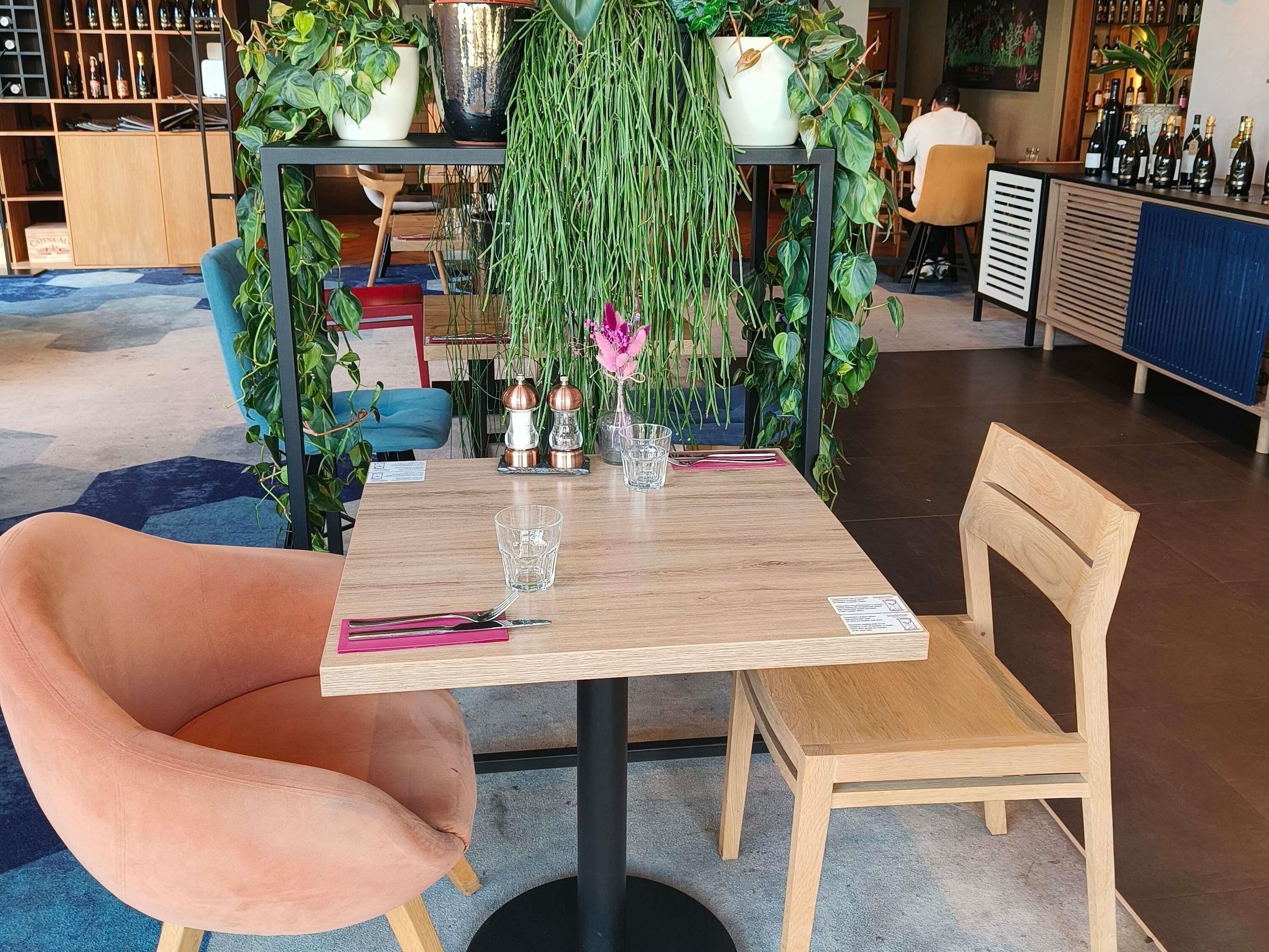 Ein Essbereich mit Tisch für zwei Personen, umgeben von Topfpflanzen und einer Bar im Hintergrund.
