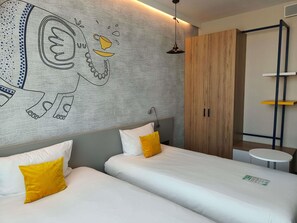 A hotel room with two beds, a wooden wardrobe, a small round table, and a wall mural.