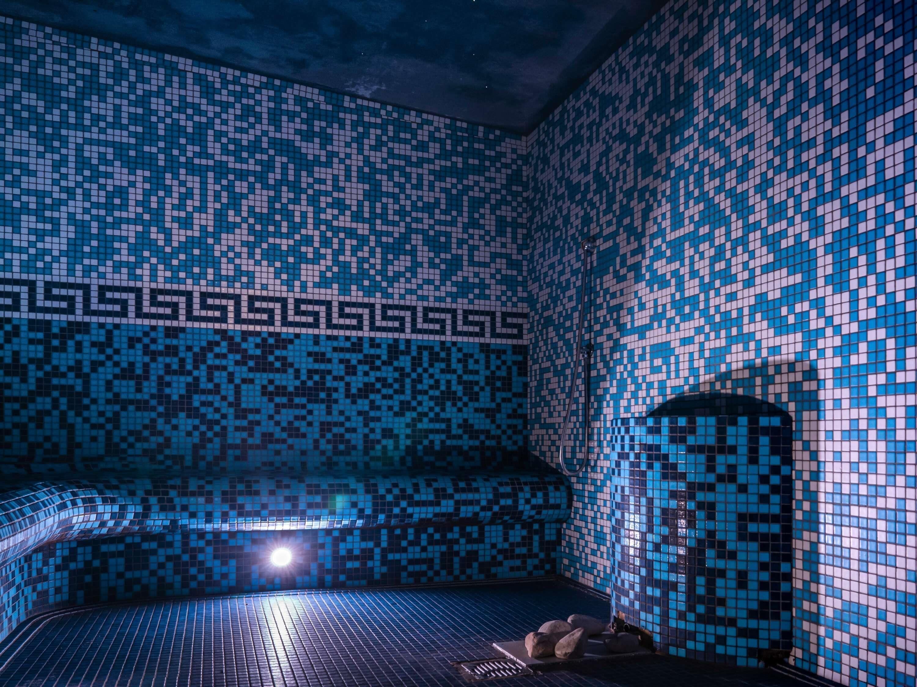 Una habitación con un muro de azulejos estampados, un banco y un objeto cilíndrico.