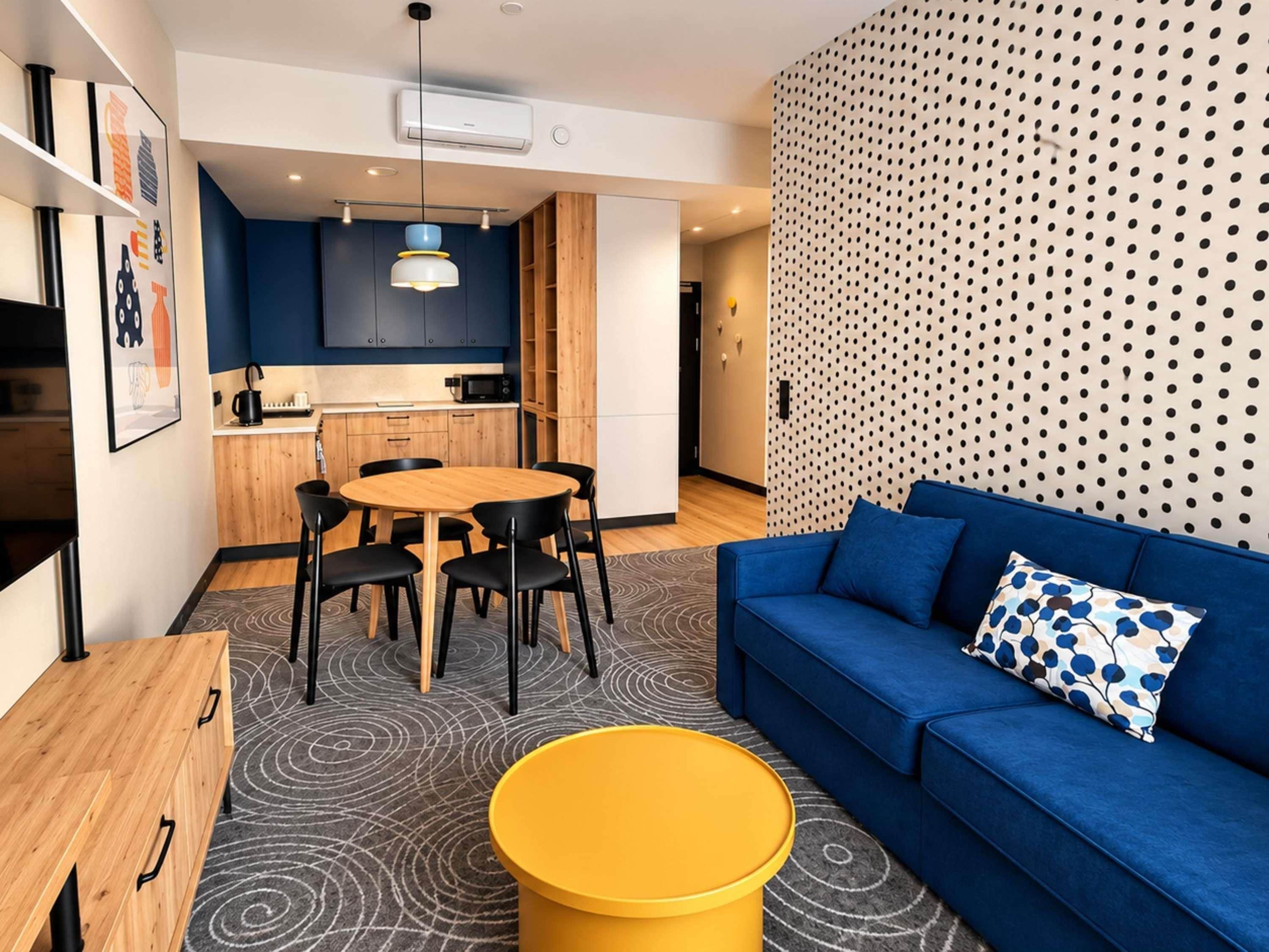 A modern living space with a blue sofa, a wooden dining table, and a kitchen area with blue cabinets.
