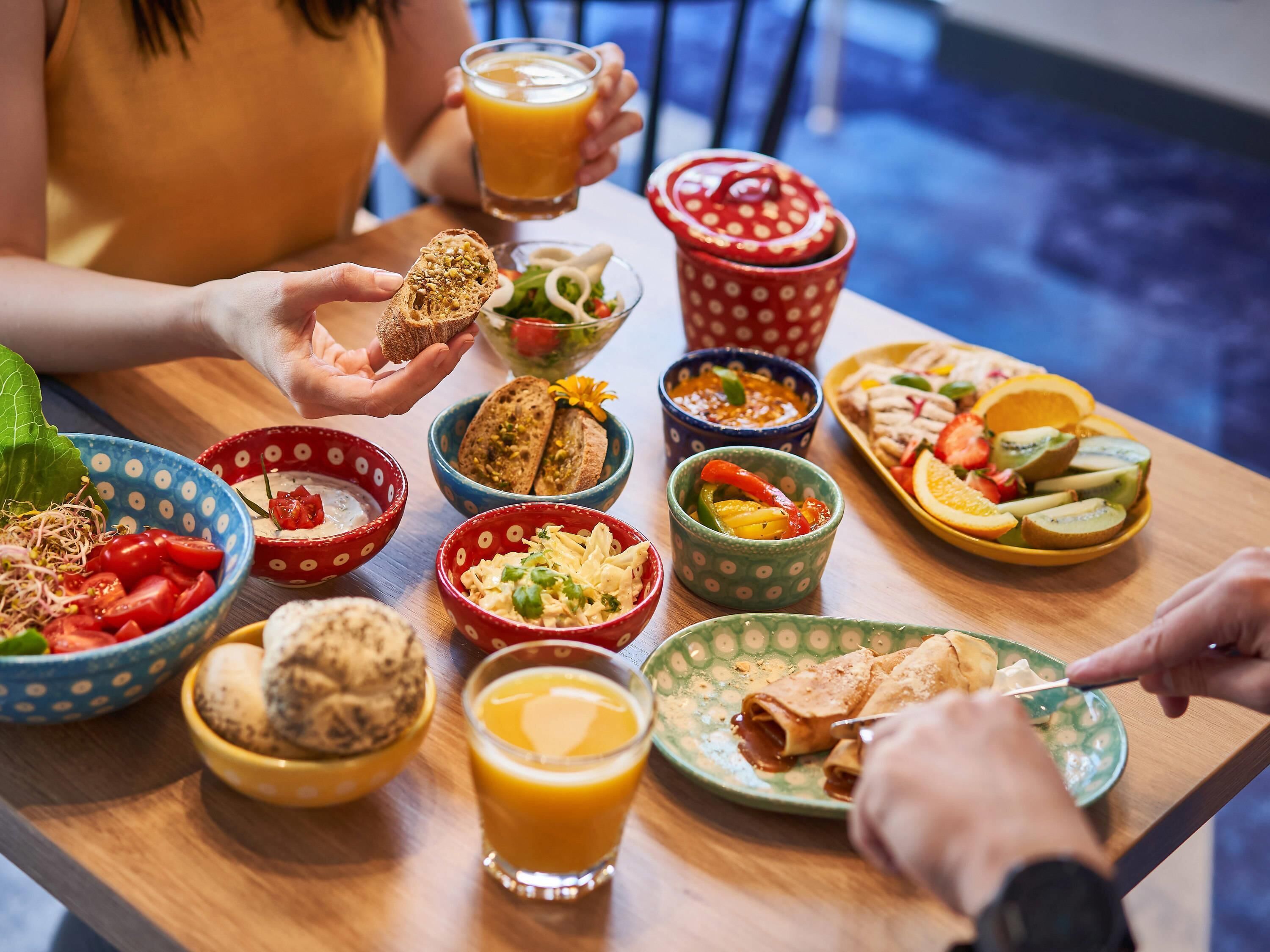A table with various food items and drinks, including bowls of salad, bread, and fruit.