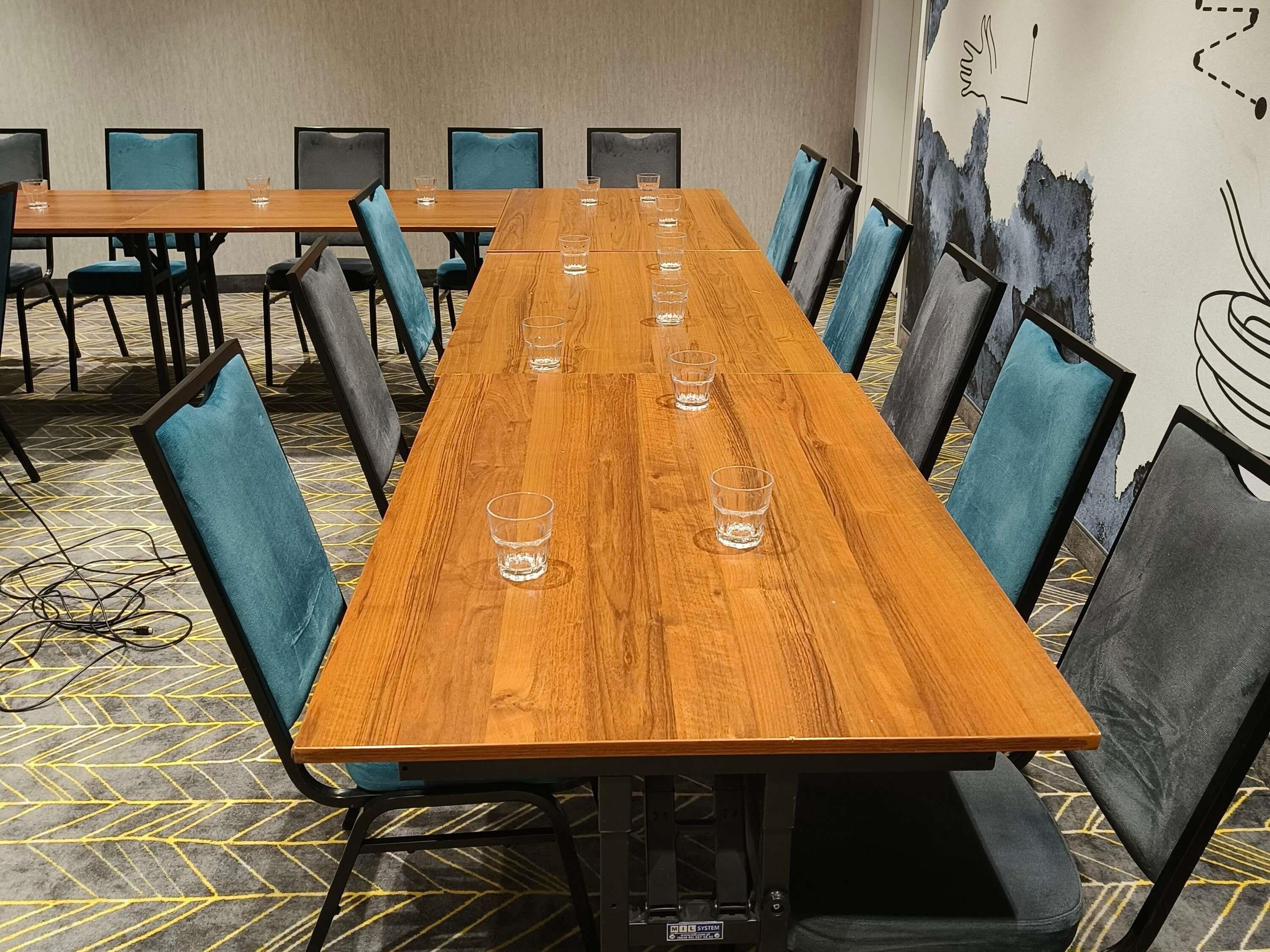 A conference room with a long wooden table, blue upholstered chairs, and a patterned carpet.