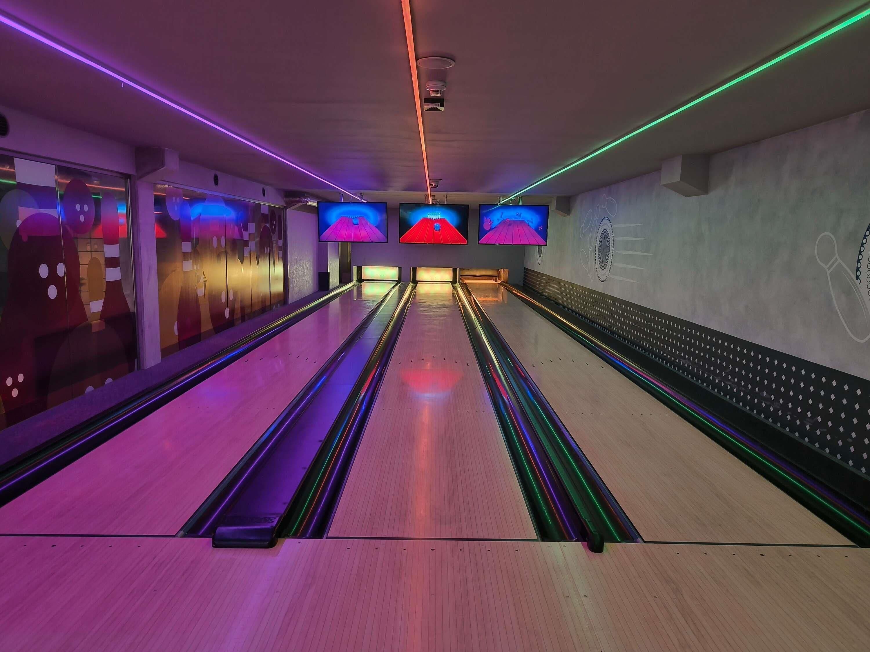 A bowling alley with multiple lanes, overhead lights, and a wall with bowling-themed decorations.