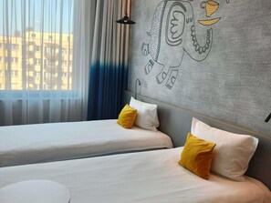 Una habitación de hotel con dos camas, una ventana con cortinas translúcidas y una pared con diseño geométrico.