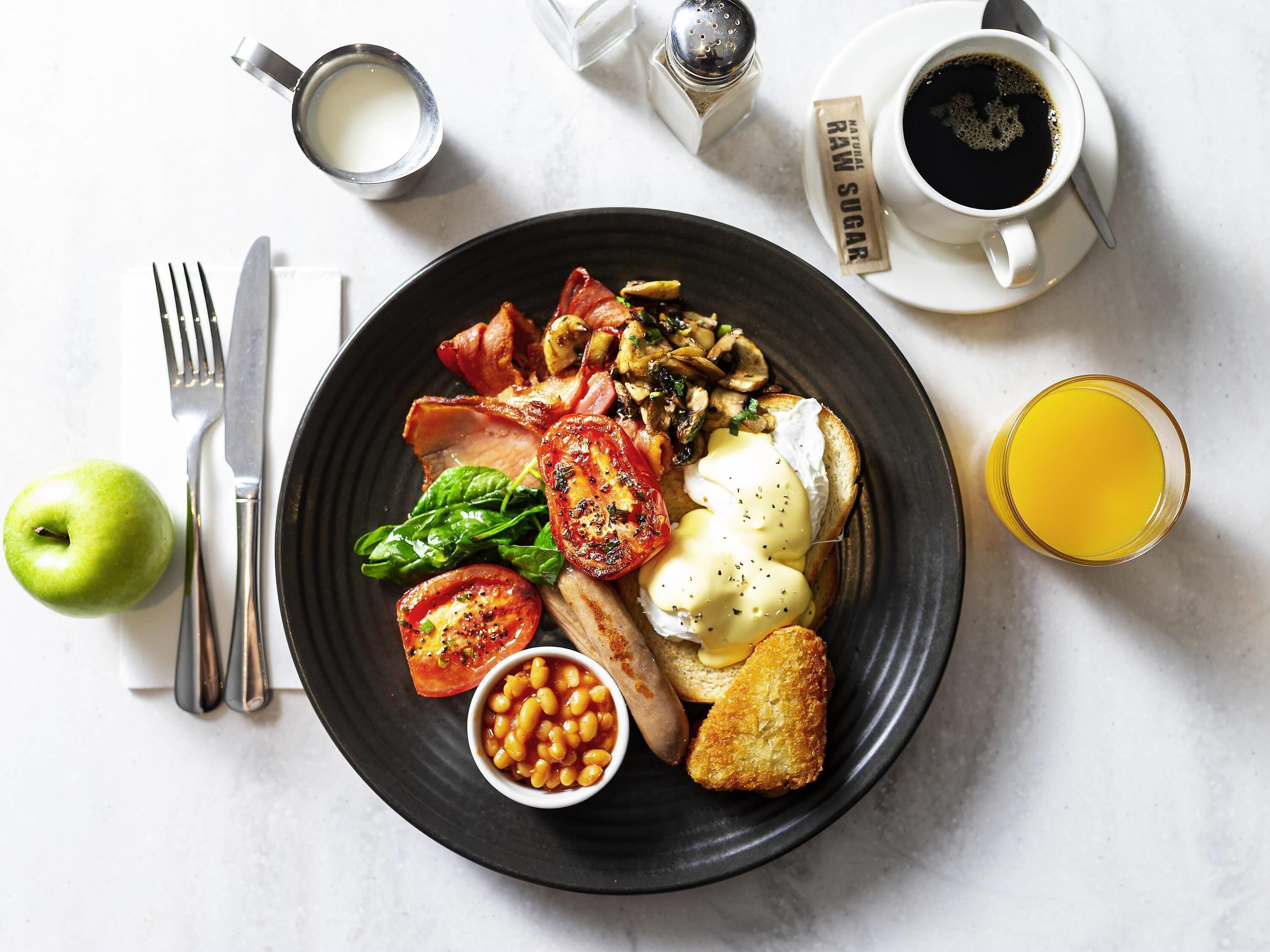 A breakfast plate with eggs, bacon, mushrooms, tomatoes, spinach, beans, toast, and a glass of orange juice.