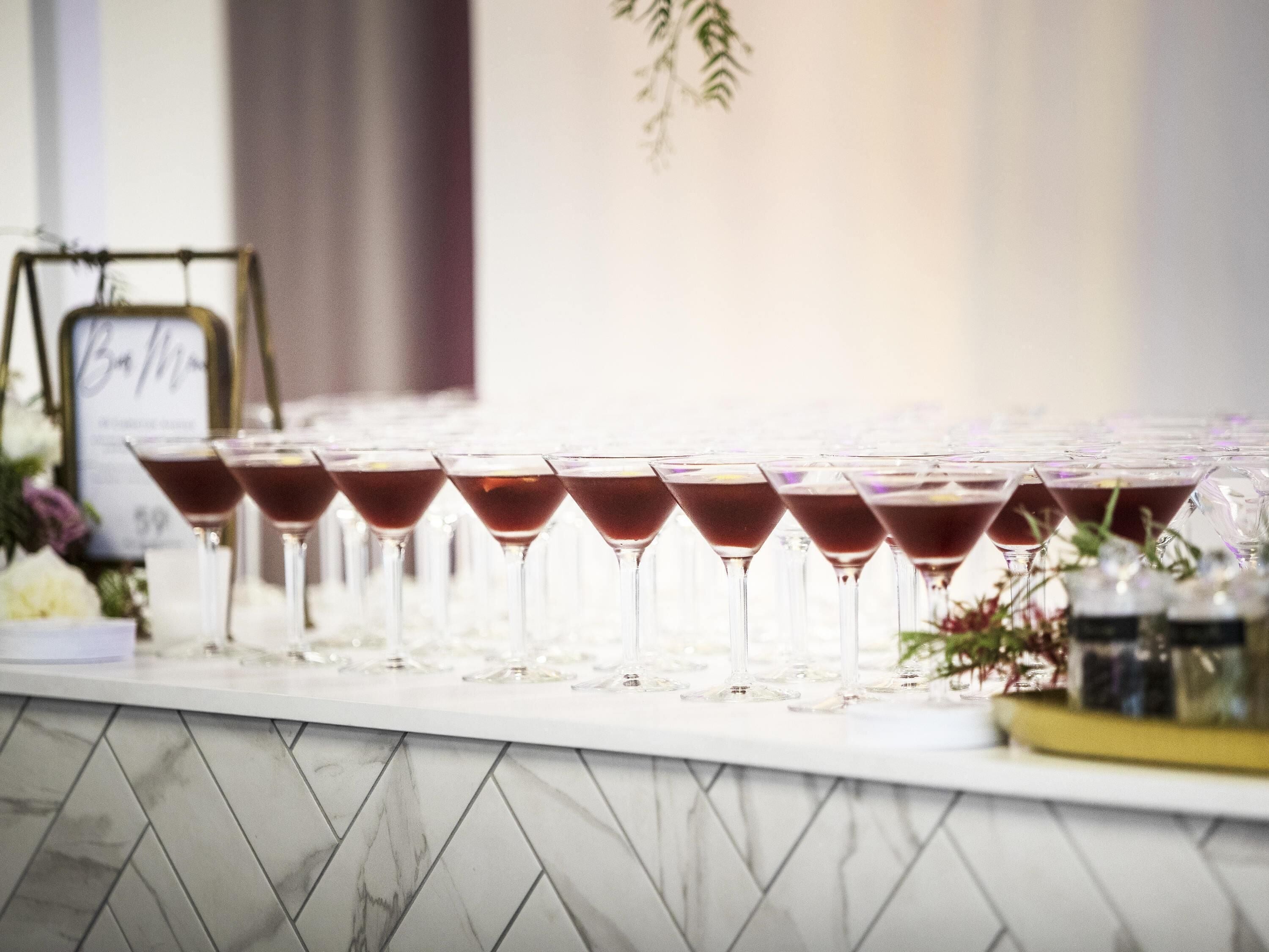 A row of martini glasses filled with a dark liquid, arranged on a marble-tiled bar counter.