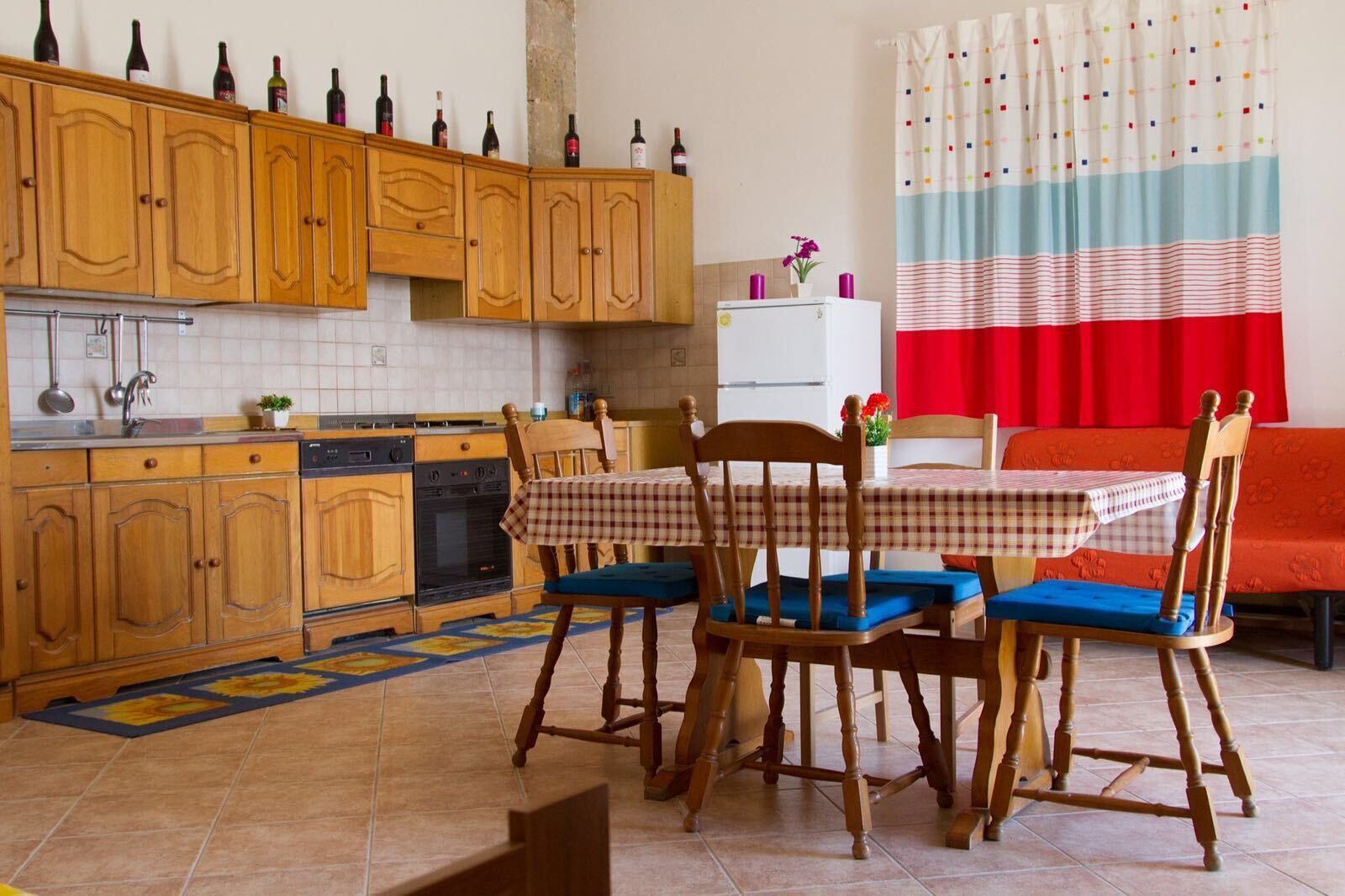 A kitchen with wooden cabinets, a dining table with checkered tablecloth, and a red sofa.
