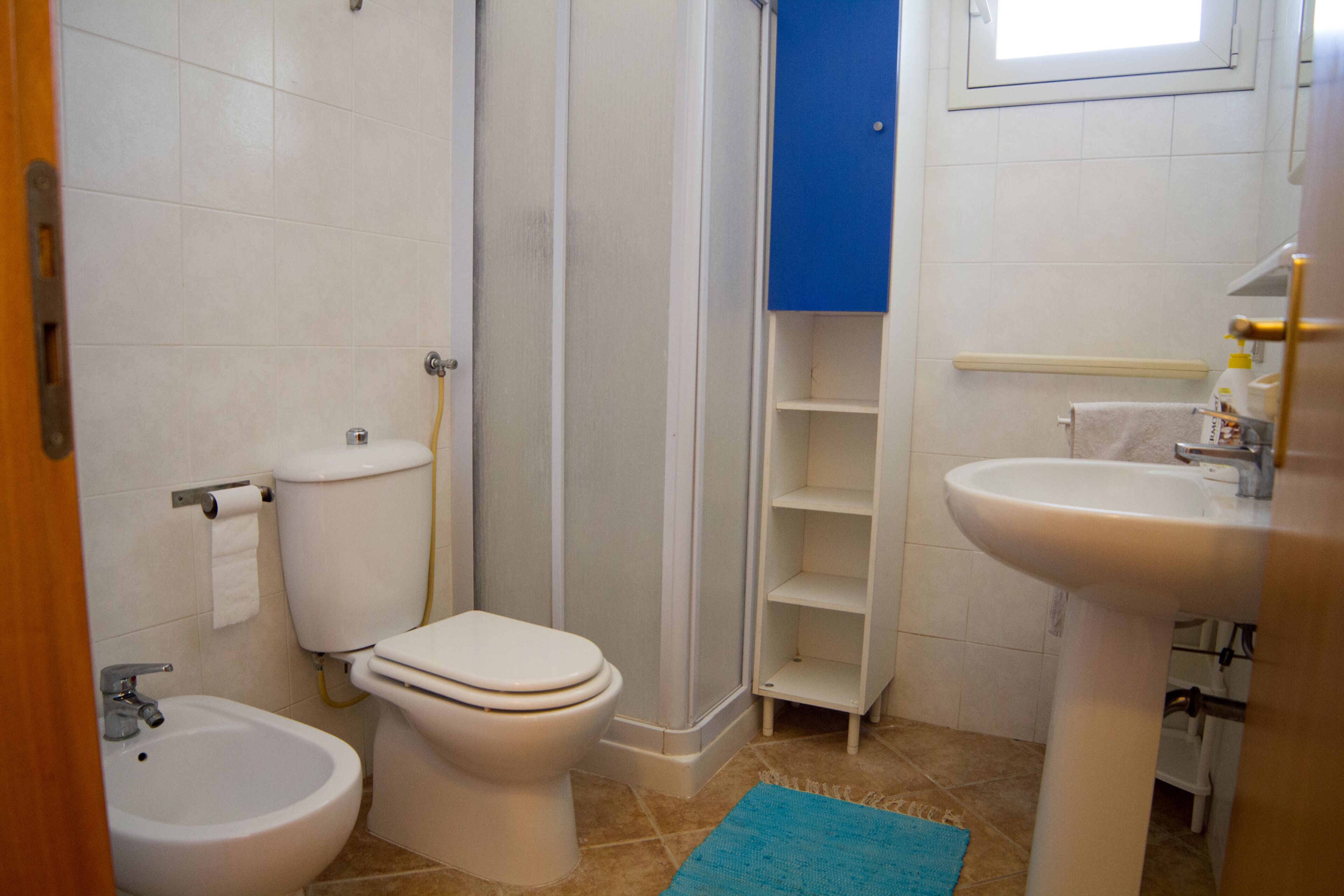 Une salle de bain équipée de toilettes, d’un bidet, d’un lavabo et d’un tapis bleu.