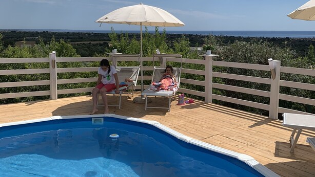 Een zwembadterras met houten dek, ligstoelen en parasols.