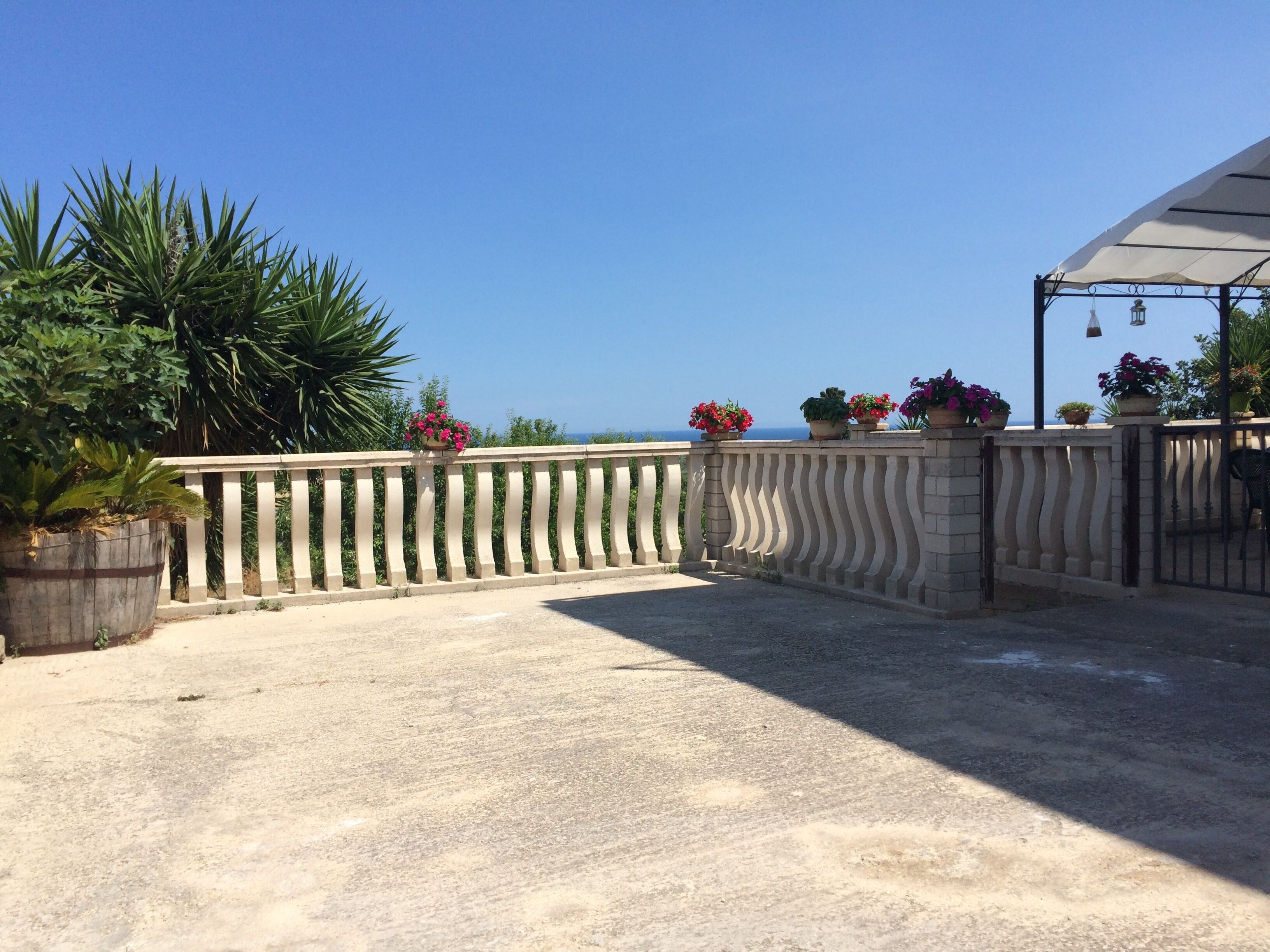 A balcony with a view of the sea, potted plants, and a pergola.