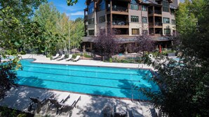 Un hotel de varios pisos con piscina, mobiliario exterior y un telón de fondo de bosque.