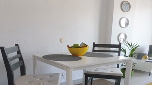 A dining area with a white table, two black chairs, a yellow bowl with fruits, and a potted plant. - KC home abroad (Playa de las Americas)