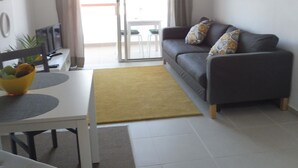 A living room with a sofa, a dining table, and a yellow rug. - KC home abroad (Playa de las Americas)
