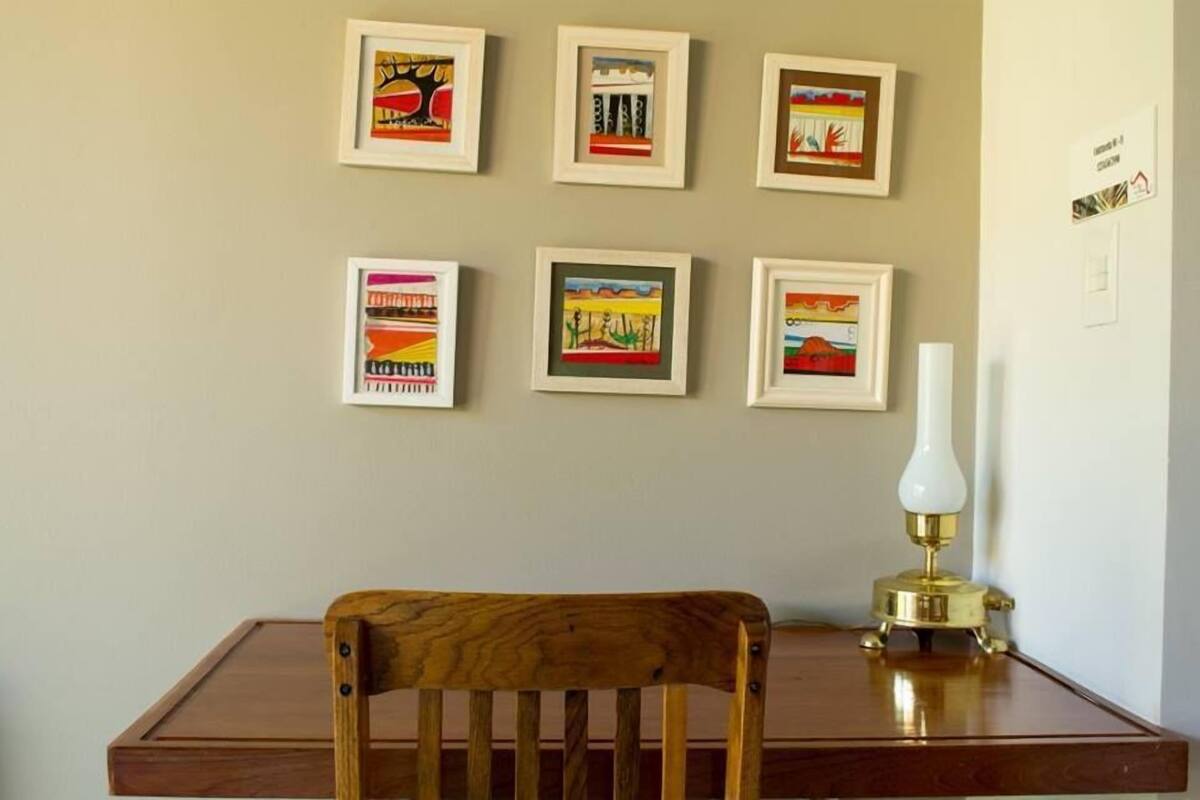 A room with a wooden chair, a table, and six framed artworks on the wall.