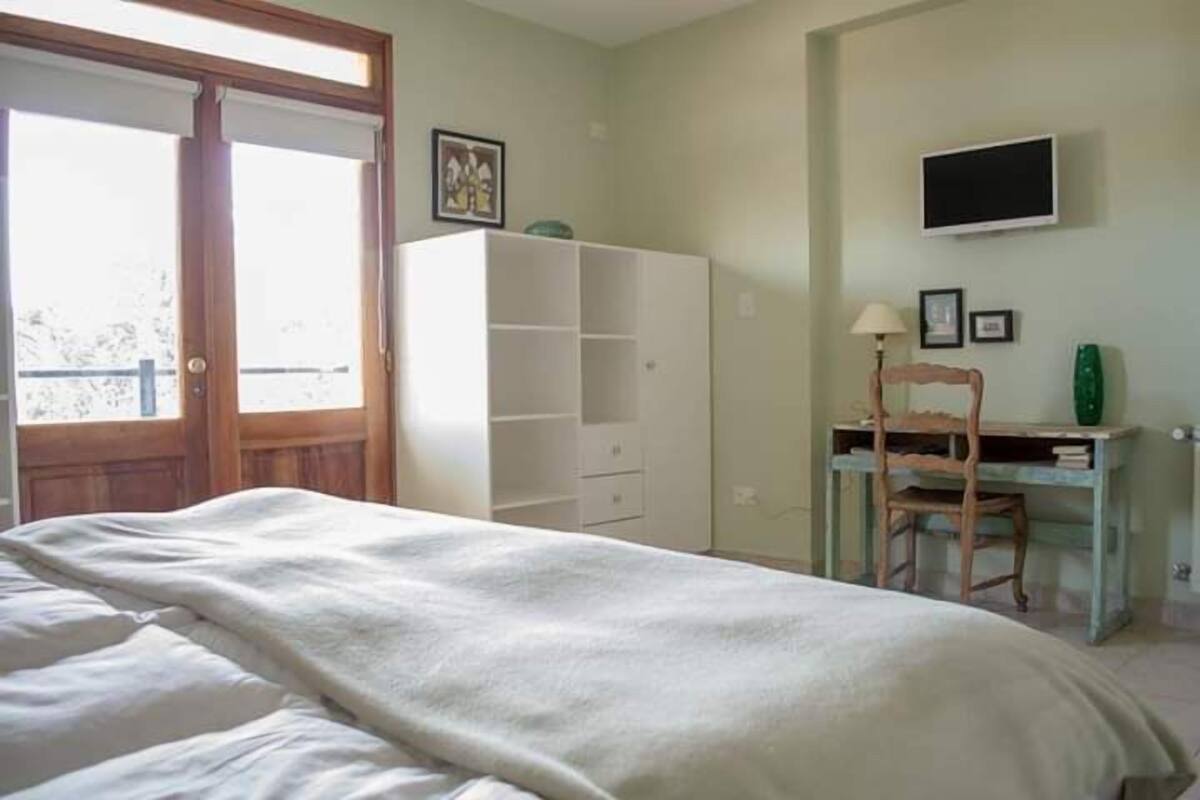 A bedroom with a bed, a wardrobe, a desk with a chair, and a television on the wall.