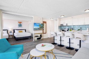 Una habitación de hotel moderna con una cama, un escritorio, una silla, una mesita y una zona de cocina con barra.